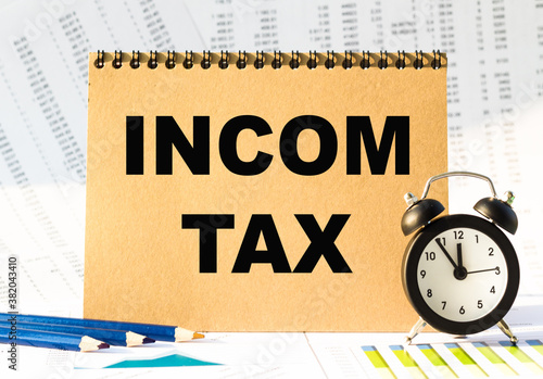 Notebook, pencils and clocks on the table with financial papers. your text INCOM TAX photo