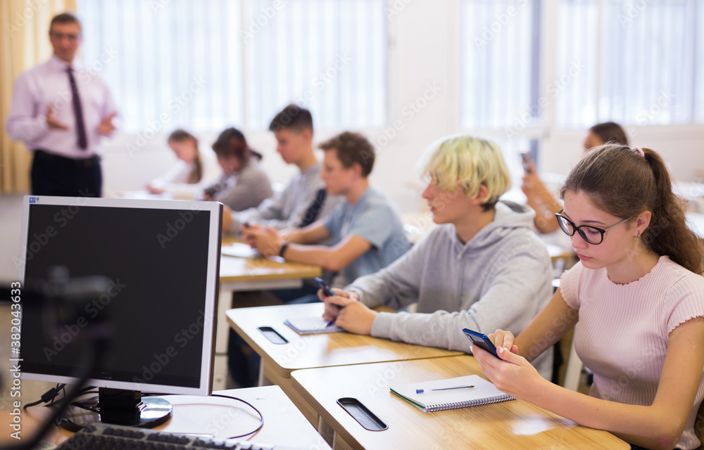 Teen students using smartphones to find necessary information on lecture in college class