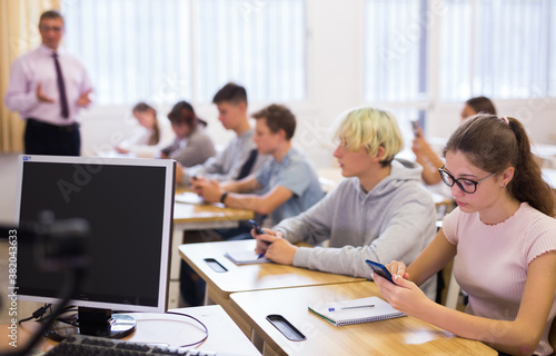 Teen students using smartphones to find necessary information on lecture in college class