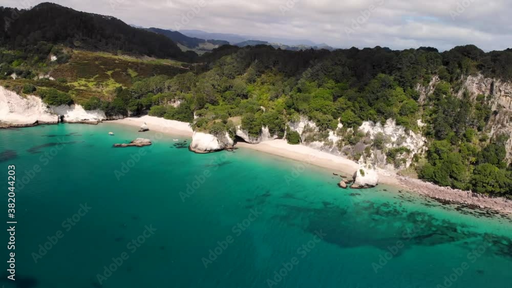 Beautiful white sandy beach throught tunnel cave surrounded limestone cliffs and forested hills at New Zealand seaside aerial orbit reveal shot. Cathedral Cove. Beautiful white sandy beach throught tunnel cave surrounded limestone cliffs and forested hills at New Zealand seaside aerial orbit reveal shot. Cathedral Cove.