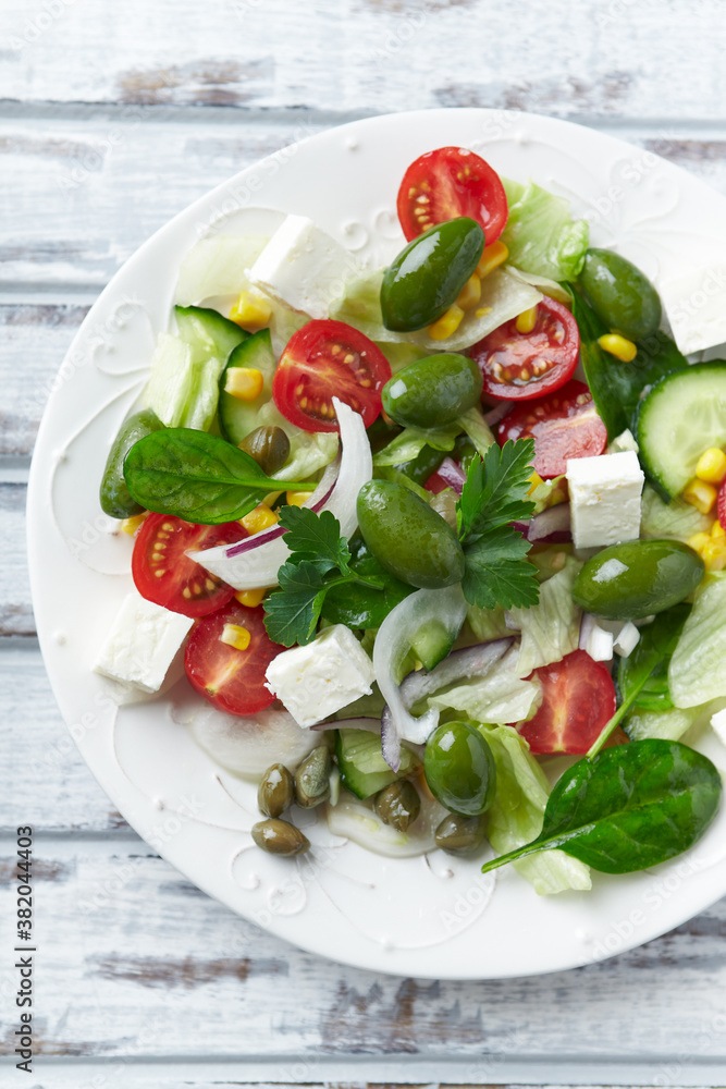 Healthy Salad with Feta Cheese, Green Olives, Baby Spinach, Cucumber, Cherry Tomatoes and Capers. Bright wooden background. Top view. Close up. Healthy Salad with Feta Cheese, Green Olives, Baby Spinach, Cucumber, Cherry Tomatoes and Capers. Bright wooden background. Top view. Close up.