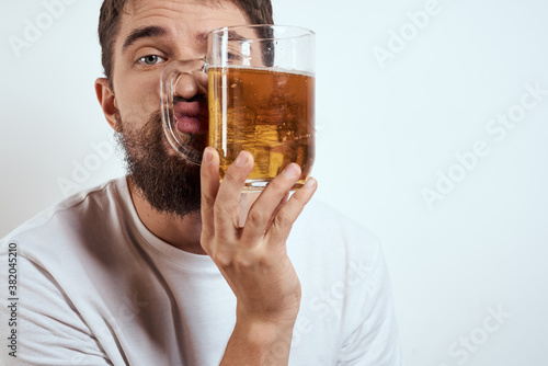 A bearded man with a mug of beer on a light background in a white T-shirt cropped view of an alcoholic drink