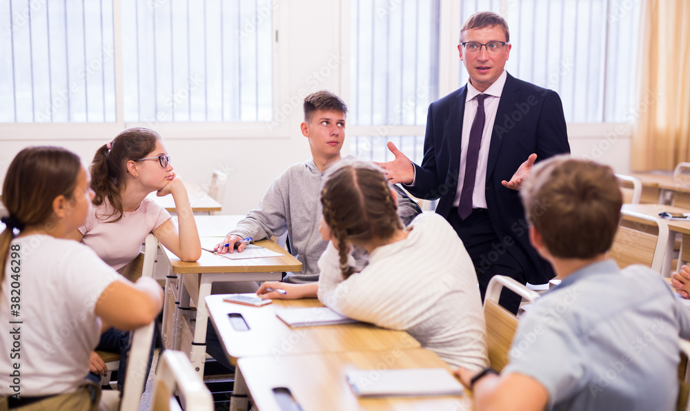 Smiling male lecturer explaining new theme and helping teenage students during class