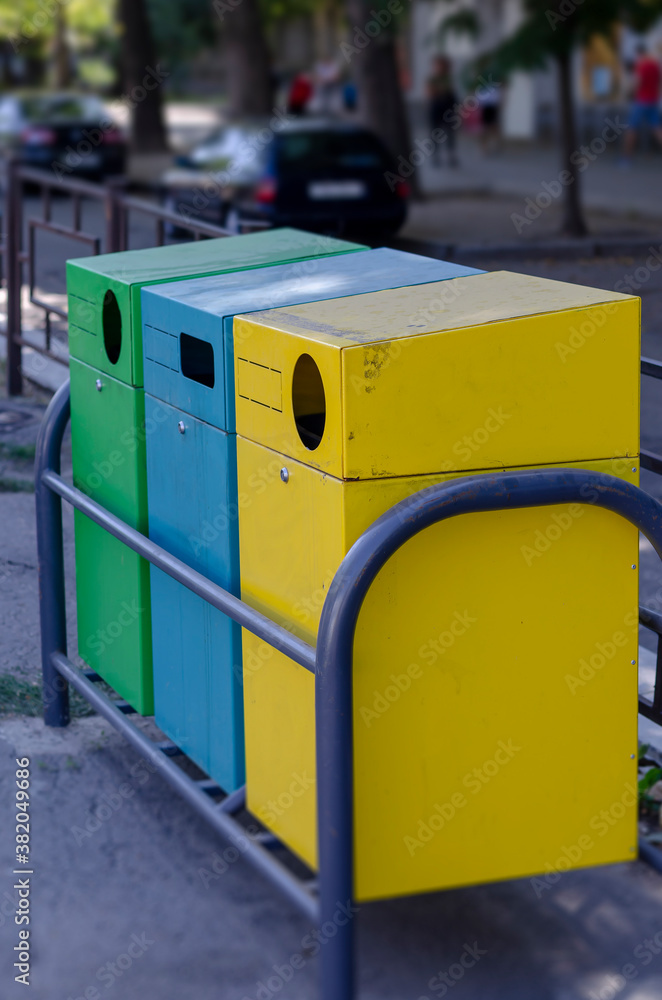 Three multi-colored garbage containers on a city street.