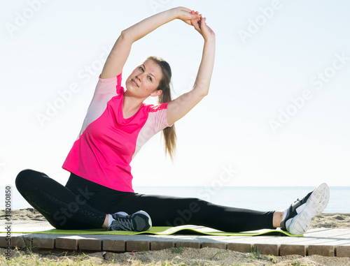 Young woman exercising yoga poses on sunny beach by ocean