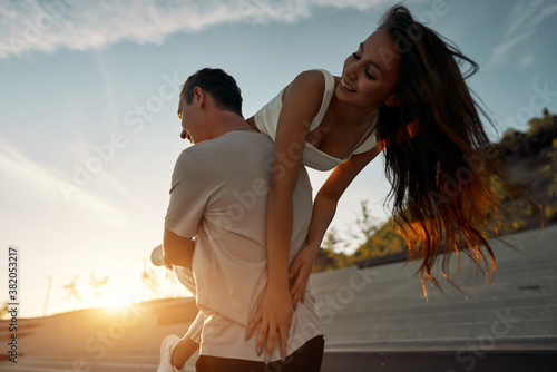 Happy couple. Man carrying woman on his back. On the Sunset