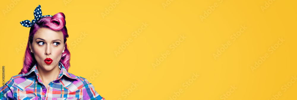 Excited surprised woman. Pinup girl looking sideways. Purple head model at retro fashion and vintage studio concept Yellow orange colour background with copyspace for some text Wide banner composition