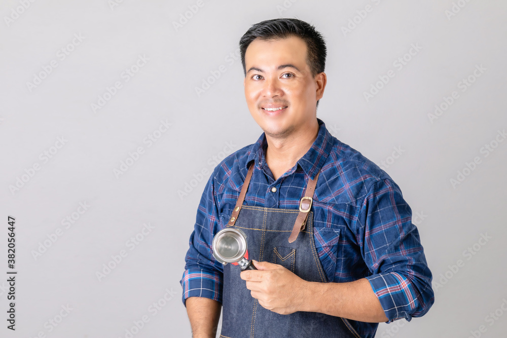 Portrait Asian man in barista uniform holding Coffee Bottomless Portafilter in studio isolated on grey