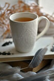 White cup of tea on the windowsill with books and white knit blanket
