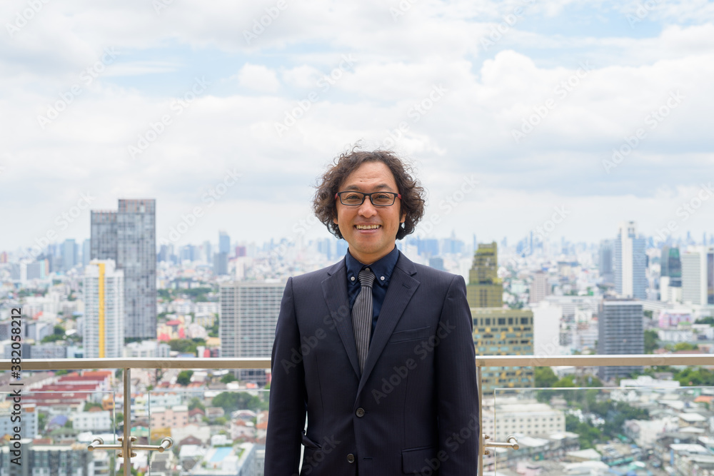 Happy Japanese businessman with curly hair smiling against view of the city