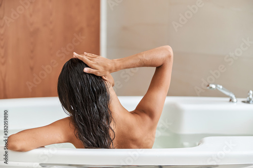 Brunette young woman touching her hair while taking bath