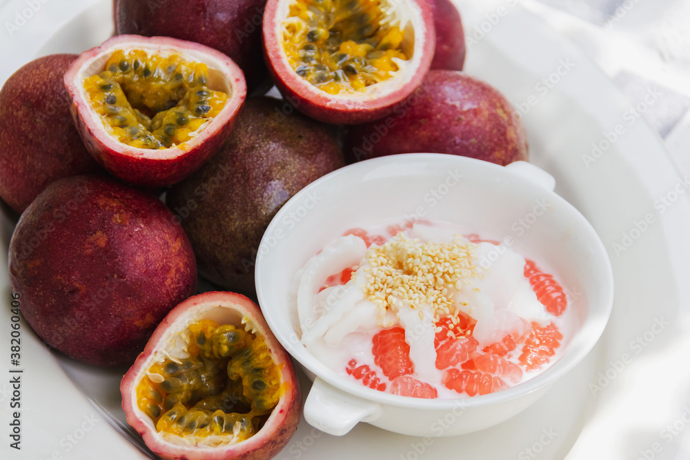 Thai dessert call krong krang made from passion fruit and flour, topped with fresh coconut water, sprinkled with sesame seeds in white cup,and fresh passion fruit placed side