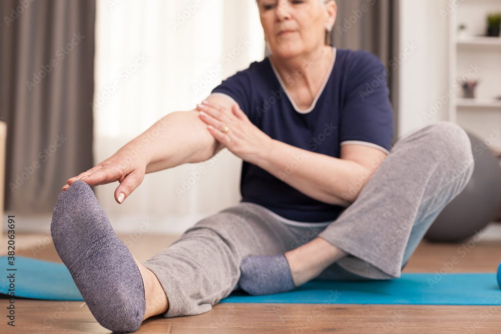 Modern grandmother doing stretching at home oon yoga mat. Old person pensioner online internet exercise training at home sport activity with dumbbell, resistance band, swiss ball at elderly retirement