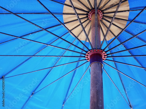 Inside of a large blue umbrella. Spokes and metal buckets support the canvas of the umbrella. Selective focus