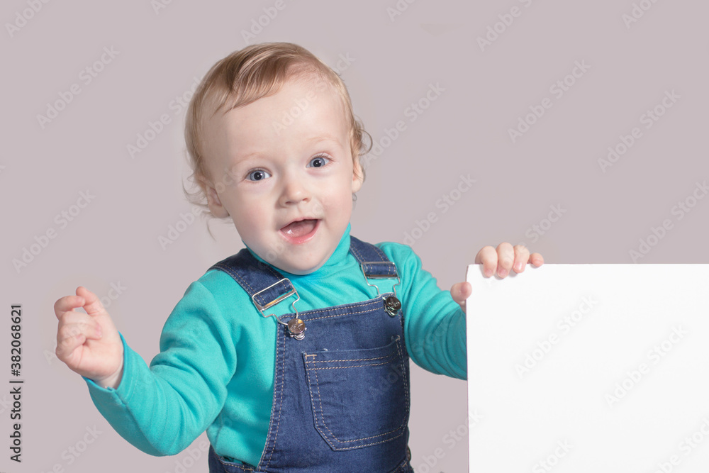The little boy smiling with a white sign on a gray background. The little boy smiling with a white sign on a gray background.
