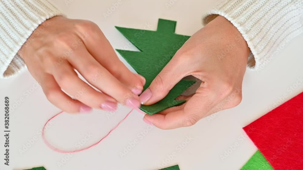 Woman hands sew two Christmas trees cut out of green fabric using red thread Woman hands sew two Christmas trees cut out of green fabric using red thread