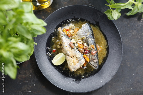 Roasted mackerel. Whole fish served with garlic, olives, and lemon. Appetizing dish served on a black plate .Culinary photography, food photography.