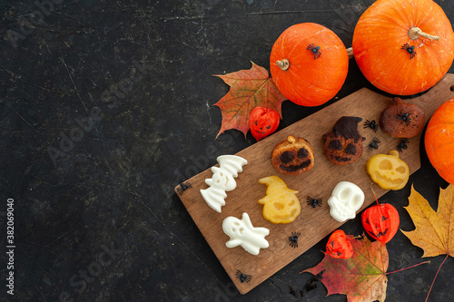 Children's fun desserts for Halloween. Muffins, panna cotta and orange jelly in the form of scary and funny characters. The composition on a dark background with pumpkins and autumn leaves. 