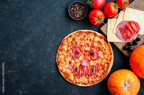 Pumpkin pizza for a Halloween party on a dark background. Pizza decorated with a scary face. Children's holiday food.