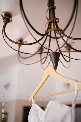 Close-up of a brown chandelier with a wooden hanger and a wedding dress on it.