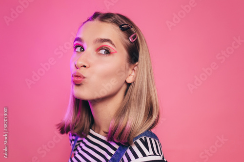 Positive amazing young caucasian woman blowing a kiss to someone and looking away. Isolated over pink background. Lips in a tubule. Bright makeup, smart casual style concept.