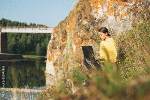 Young woman traveler freelancer in yellow hoodie with opened laptop on the beautiful view background photo