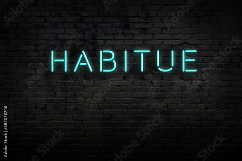 Night view of neon sign on brick wall with inscription habitue photo