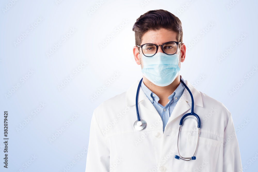 Portrait of male doctor while wearing face mask while standing at isolated background
