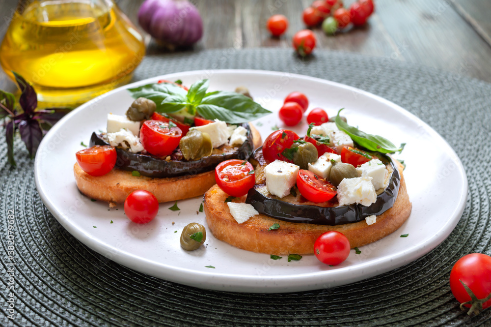 Garlic bruschetta with eggplant, feta, cherry tomatoes, capers. Useful vegetarian appetizer. Italian Cuisine. Garlic bruschetta with eggplant, feta, cherry tomatoes, capers. Useful vegetarian appetizer. Italian Cuisine.