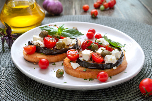 Garlic bruschetta with eggplant, feta, cherry tomatoes, capers. Useful vegetarian appetizer. Italian Cuisine. © yaroshenko