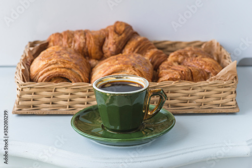Fototapeta Naklejka Na Ścianę i Meble -  Traditional french breakfast. Vintage green cup of coffee and basket with hot croissants on white table