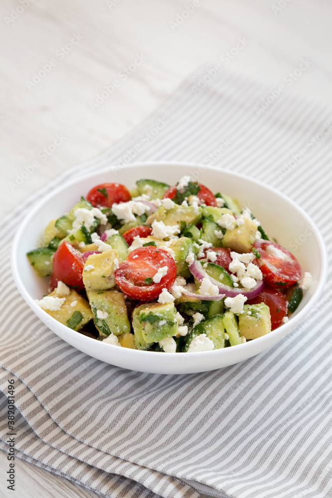 Tasty Avocado Tomato and Cucumber Salad in a bowl on a white wooden surface, side view. Close-up. Tasty Avocado Tomato and Cucumber Salad in a bowl on a white wooden surface, side view. Close-up.