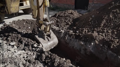 Big metal excavator bucket scoops up dirt while digging a ditch during roadworks in countryside. Ripper bucket excavating soil and rocks at a construction site on a sunny day.