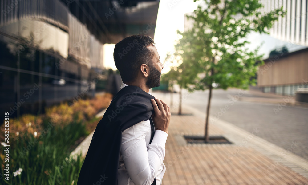 Dapper Indian businessman daydreaming looking into the distance with jacket over shoulder