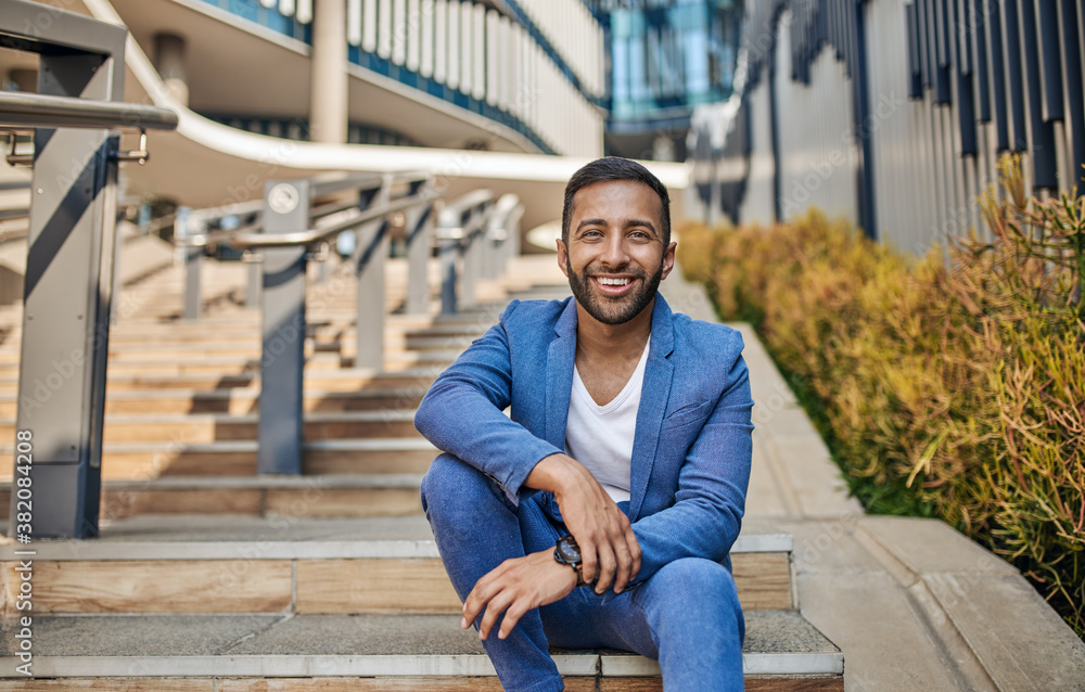 Smiling handsome Indian arabic business man sitting on outdoor city staircase Smiling handsome Indian arabic business man sitting on outdoor city staircase