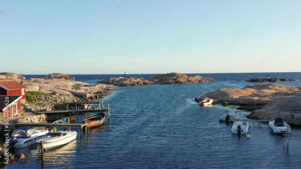 Fast moving low angle aerial drone flight on ocean channel inshore bay in Sweden. Fishing village on Sweden's west coast with blue ocean and boats at pier. Fast moving low angle aerial drone flight on ocean channel inshore bay in Sweden. Fishing village on Sweden's west coast with blue ocean and boats at pier.
