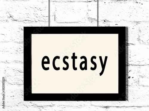 Black frame hanging on white brick wall with inscription ecstasy photo