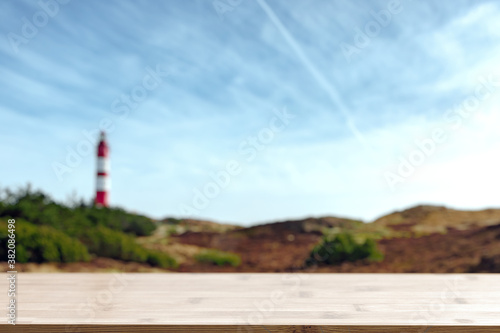 Empty wooden bar on bottom and blurred view of seaside landscape with red-white striped lighthouse. © Martin Piechotta