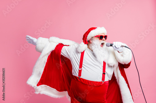 Crazy funky cool grey beard santa claus north-pole pop star celebrity sing song mic enjoy x-mas christmas eve karaoke wear sunglass cap headwear suspenders isolated pastel color background