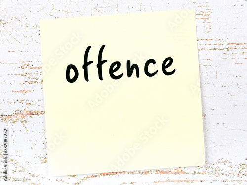 Fotografering Yellow sticky note on wooden wall with handwritten word offence