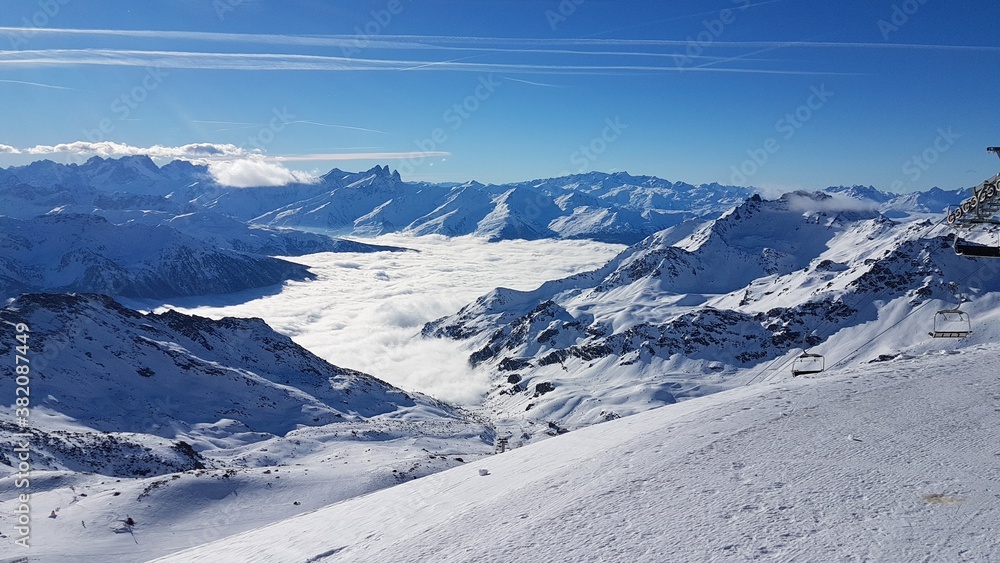 View of the snow-covered peaks of the French Alps, above a cloud cover with a sunny blue sky from the ski area Les Trois Vallees