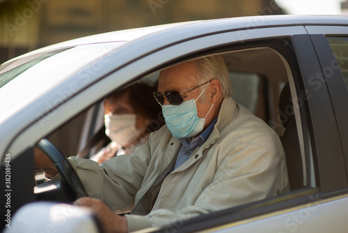 Senior couple wearing anti virus masks are driving in a car during the COVID-19 pandemic