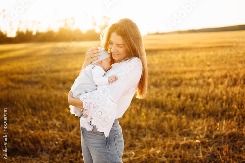 Pretty woman with cute newborn baby girl walking at the field  loving mother hold beautiful little daughter in arms  enjoy happy moments with child  maternity concept