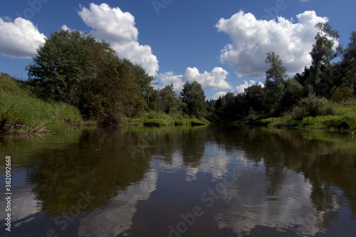 River on a summer day. A river with willows on the green banks. View from the middle of the river.