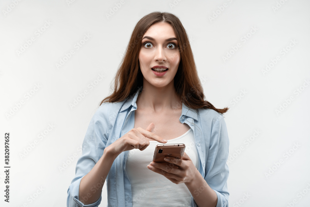 Surprised Young woman using smartphone on white background. New useful application. Studio shot, white background Surprised Young woman using smartphone on white background. New useful application. Studio shot, white background