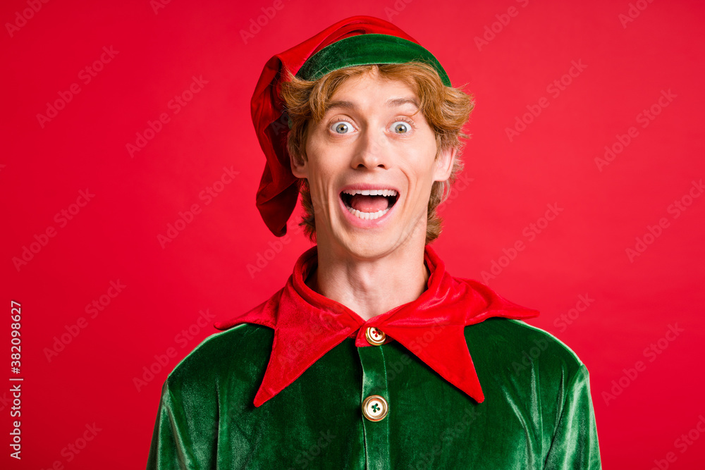 Photo of handsome guy look camera open mouth excited wear santa elf green costume headwear red color background Photo of handsome guy look camera open mouth excited wear santa elf green costume headwear red color background