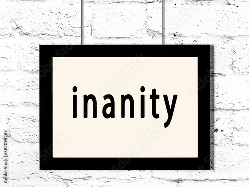 Obraz na plátně Black frame hanging on white brick wall with inscription inanity