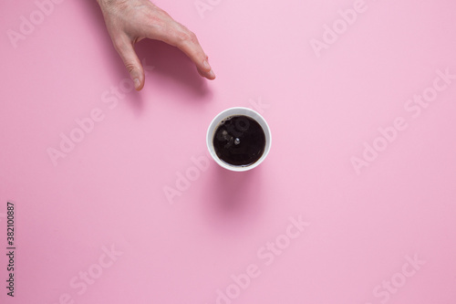 A male hand reaches for a glass with a coffee on a pink background. View from above. photo