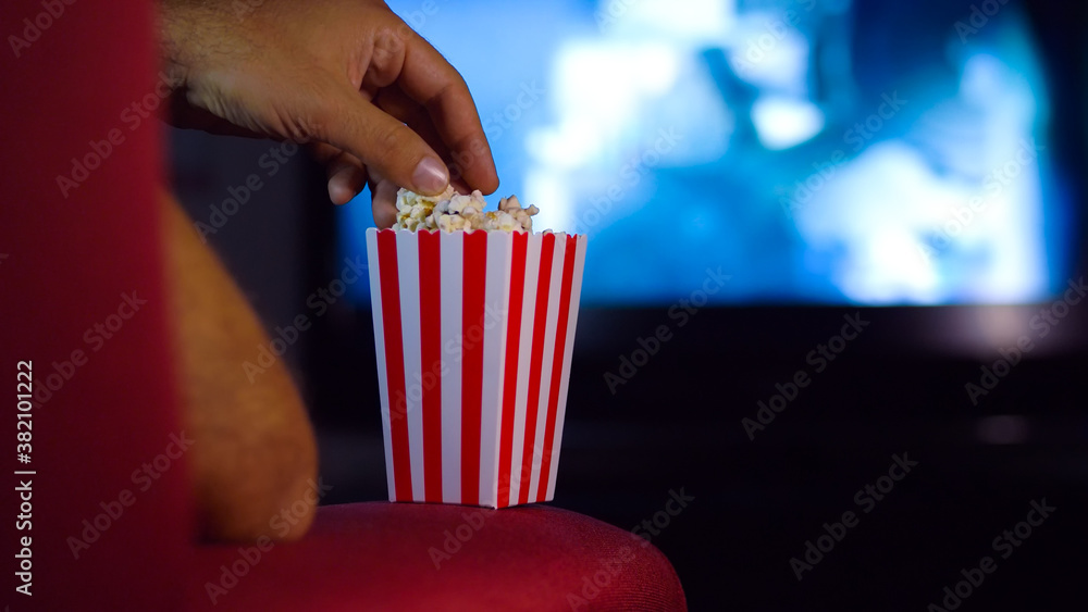 Eating popcorn while watching a movie on the couch at home. Scene in a