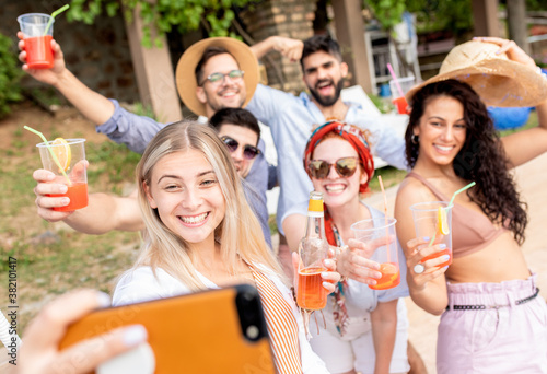 Group of young people having fun at summer vacation and enjoying a poolside party with drinks and making selfie. 